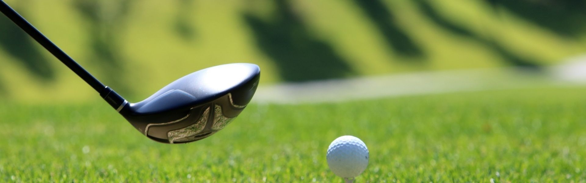 A close up of a golf driver about to this a golf ball off a tee